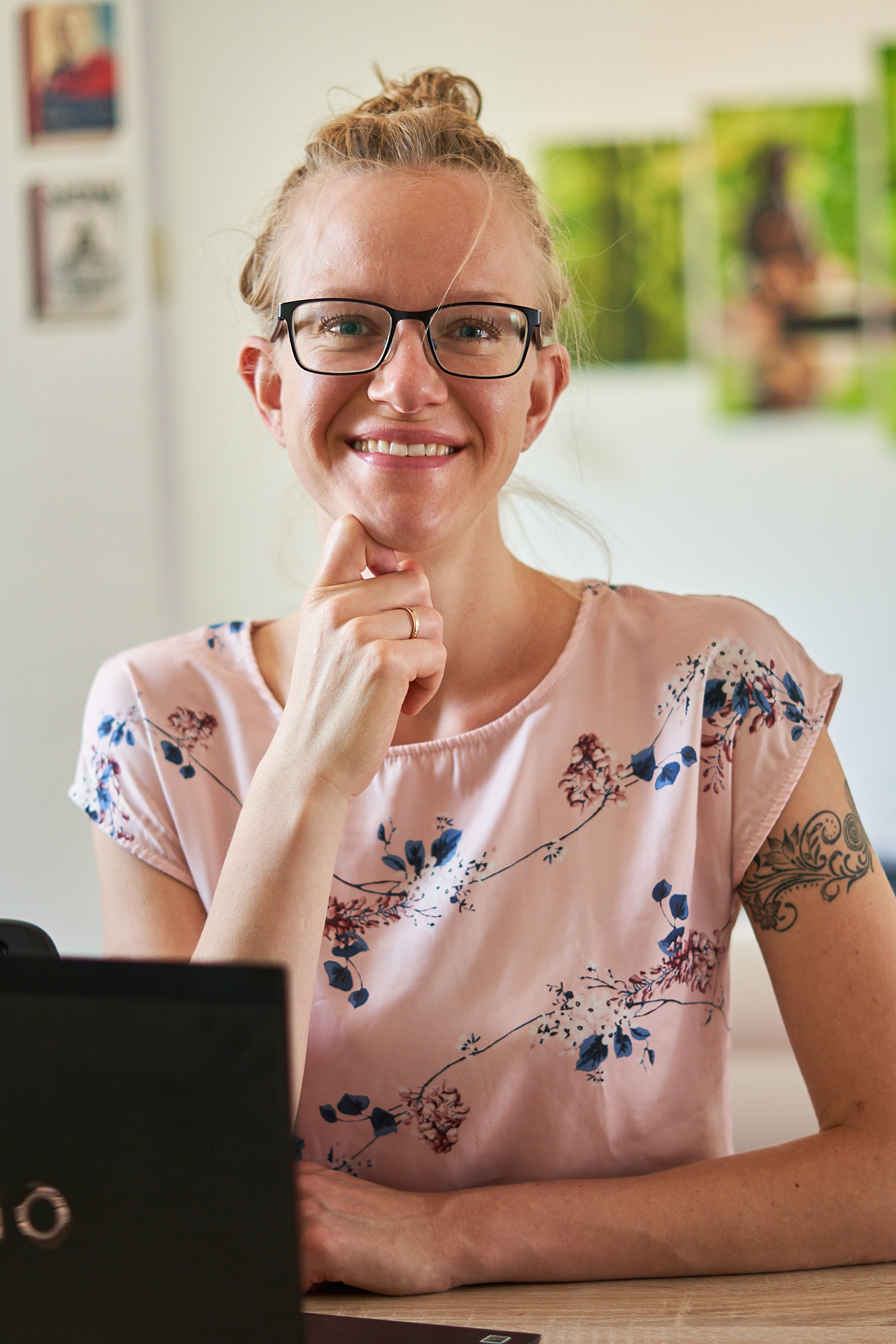 Willkommensbild für Unternehmen und Organisationen Lisa Jara, eine blonde, weiße Frau mit Dutt und rosafarbenem Oberteil sitzt am Schreibtisch und strahlt in die Kamera